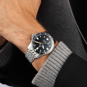 Orologio subacqueo in acciaio al polso, quadrante nero con indici verdi e lancette arancioni.