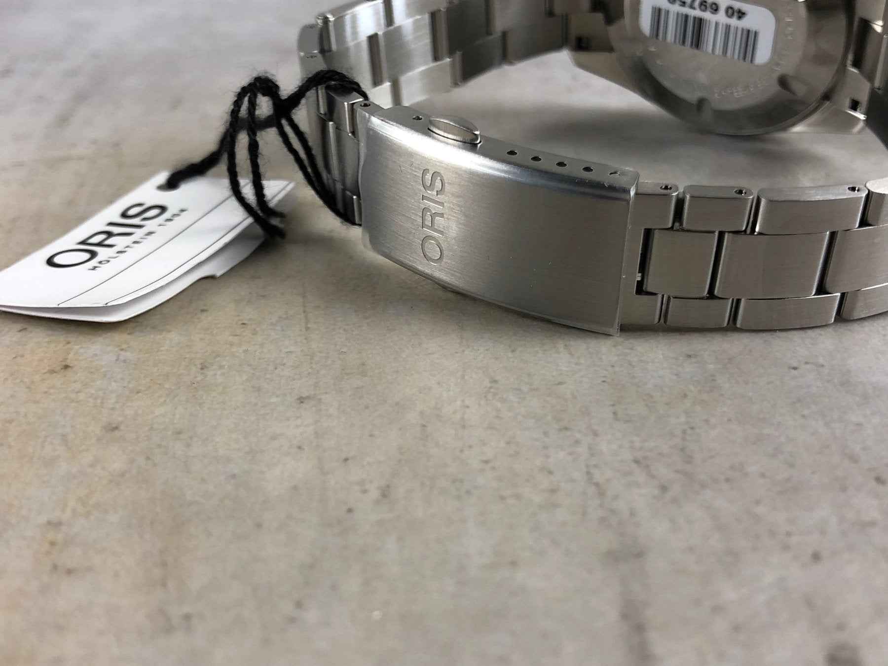 Orologio ORIS con bracciale in acciaio e fondello; tag e cinturino a maglie metalliche.