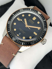 Orologio sub con lunetta nera, quadrante blu scuro, indici dorati, cinturino pelle marrone.