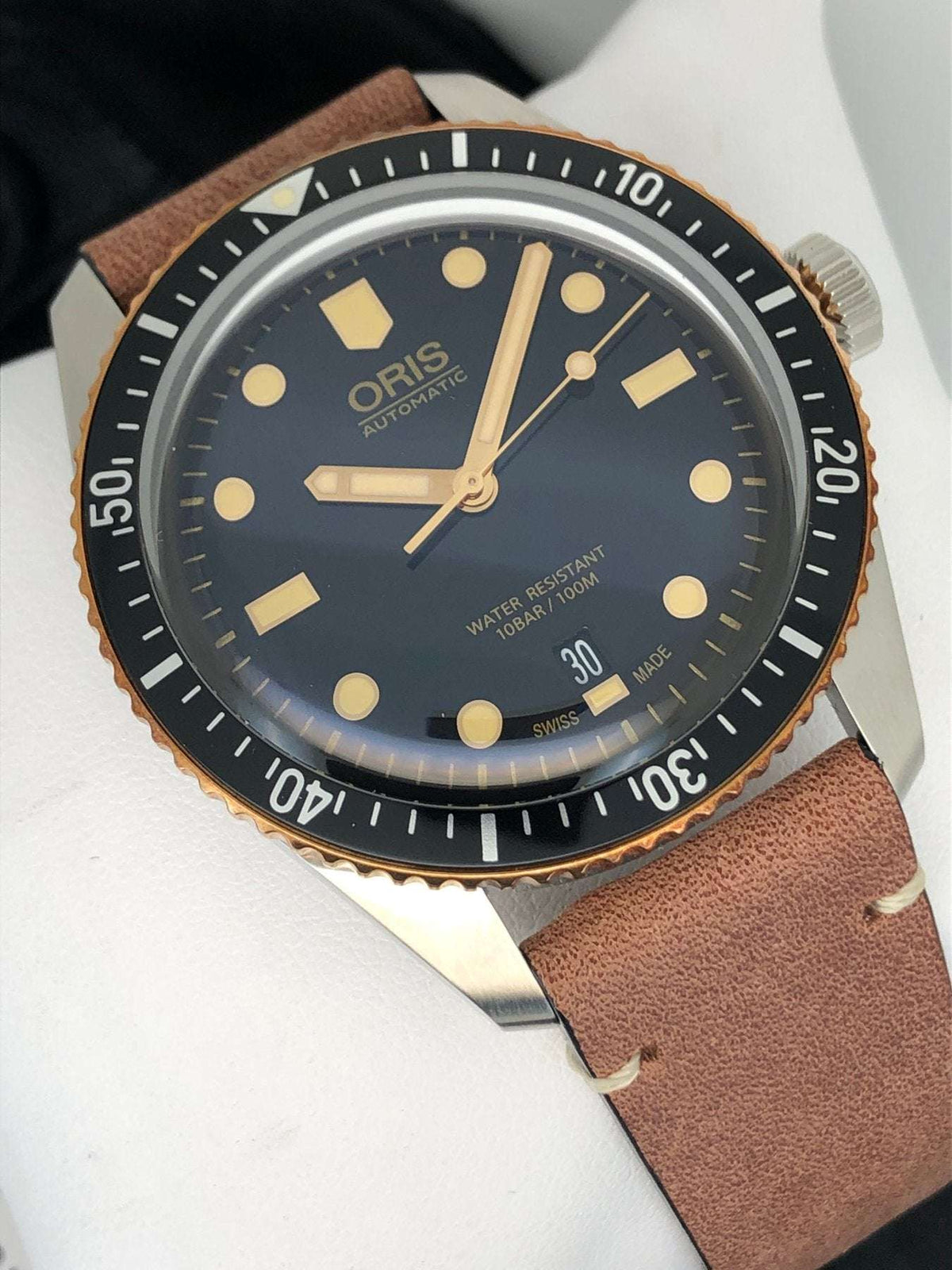 Orologio con quadrante blu scuro e datario, indici dorati, cinturino in pelle marrone.