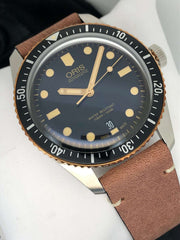 Orologio con quadrante blu scuro e datario, indici dorati, cinturino in pelle marrone.