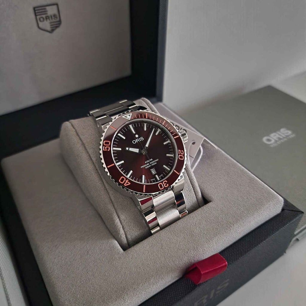 Orologio subacqueo in acciaio con quadrante marrone e lunetta rossa, su scatola