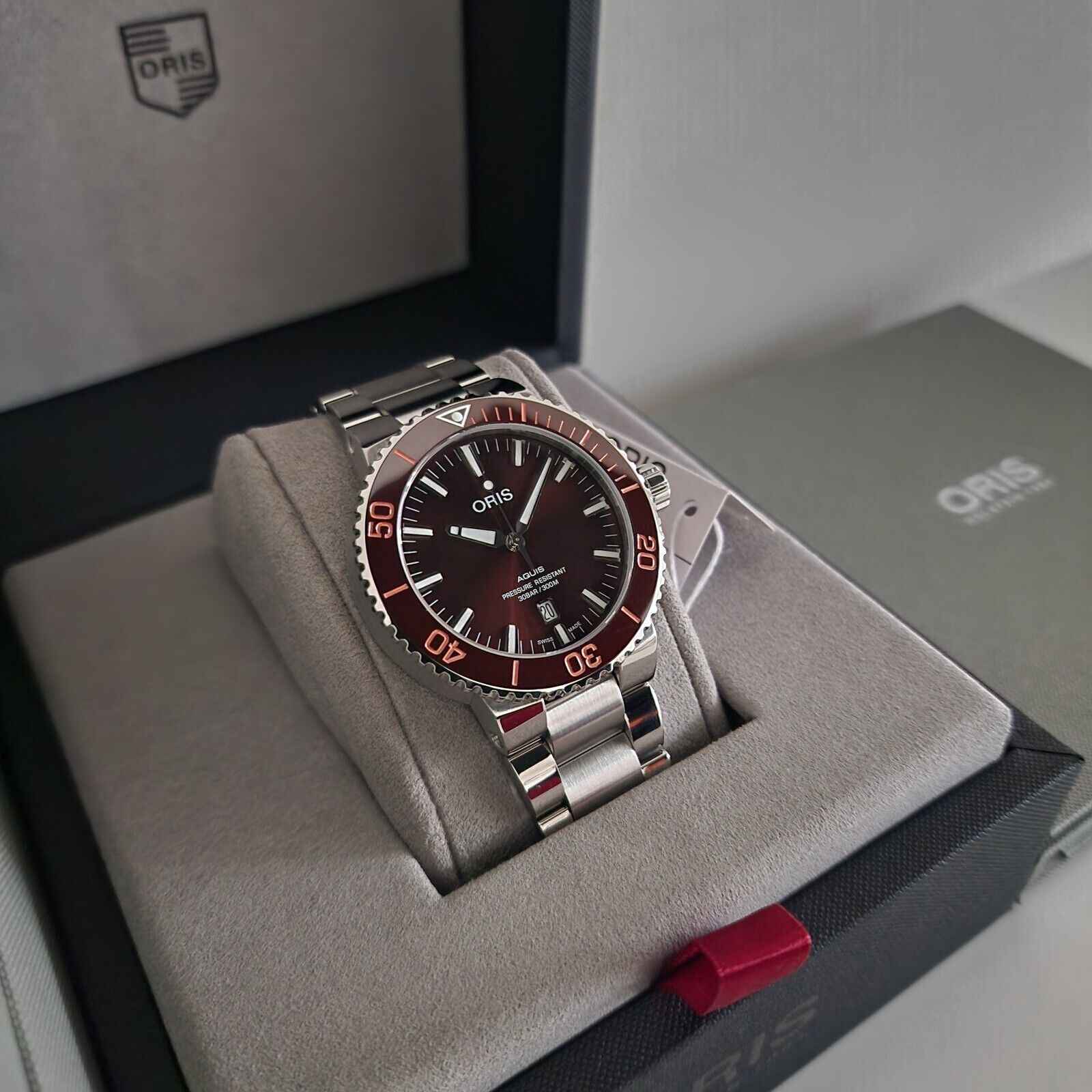 Orologio subacqueo in acciaio con quadrante marrone e lunetta rossa, su scatola