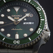 Primo piano orologio Seiko 5 Sports: quadrante verde, dettagli oro e giorno/data MON 6