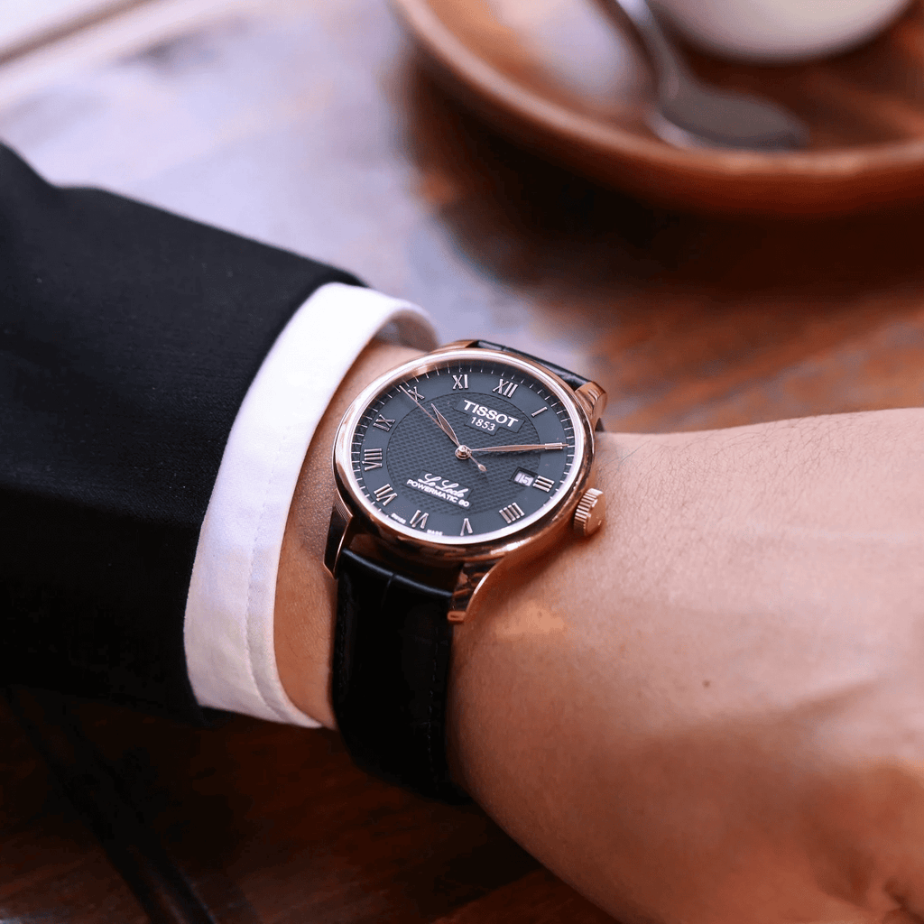 Orologio con quadrante nero e cassa oro rosa, cinturino in pelle nera su polso