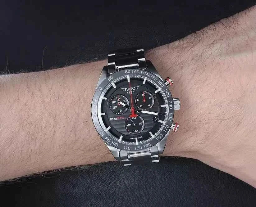 Orologio cronografo Tissot con quadrante nero e bracciale in acciaio su polso.