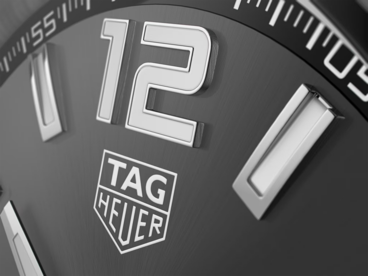 Primo piano quadrante TAG Heuer nero con logo e indici luminosi bianchi.