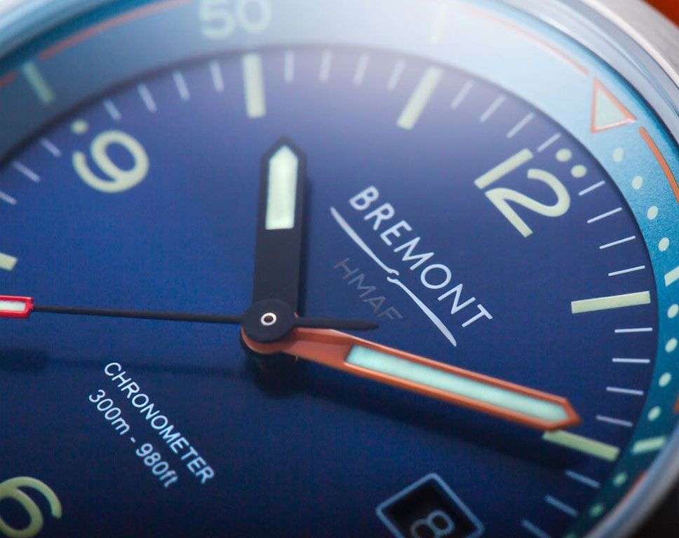 Primo piano quadrante blu: lancette arancioni e nere, indice luminoso, cinturino arancione