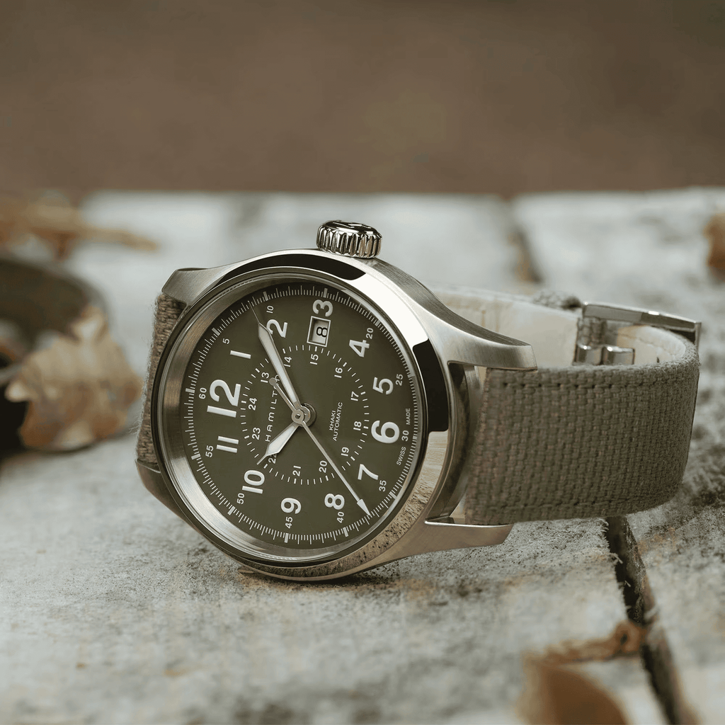 Orologio automatico con quadrante scuro e cinturino canvas verde oliva, cassa d’acciaio.