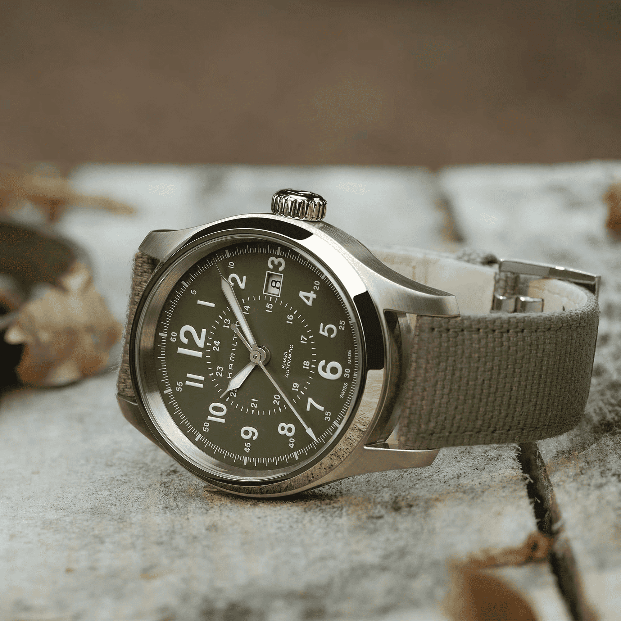 Orologio automatico con quadrante scuro e cinturino canvas verde oliva, cassa d’acciaio.