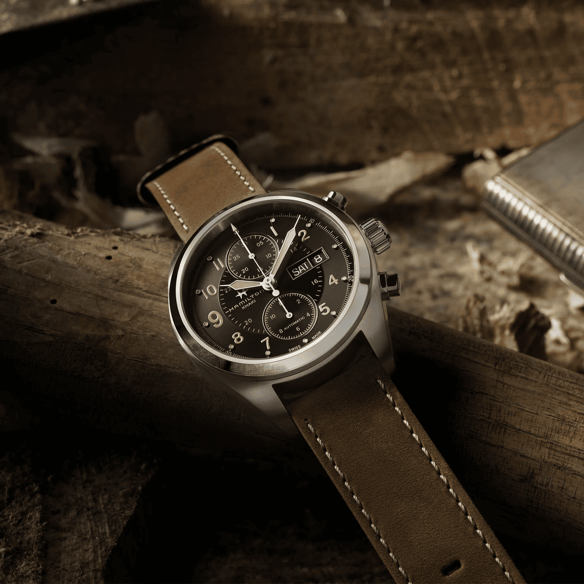 Orologio automatico con quadrante nero e cinturino in pelle kaki su superficie in legno