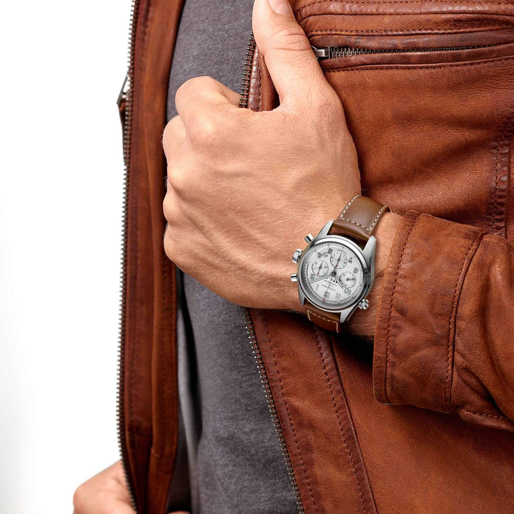 Orologio automatico al polso: quadrante argento, cinturino in pelle marrone, abito in pelle.
