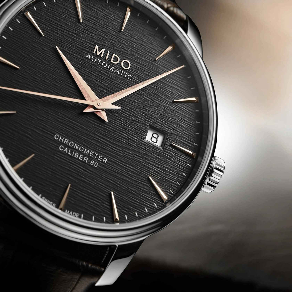 Primo piano orologio Mido automatico: quadrante nero, lancette oro rosé e datario 8