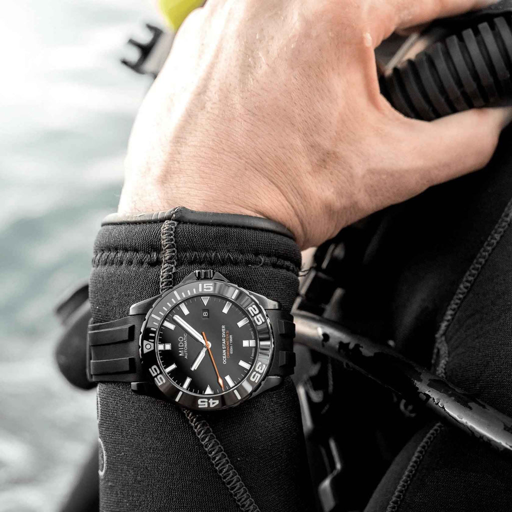 Orologio subacqueo Mido su polso, cinturino nero in silicone e quadrante nero arancione