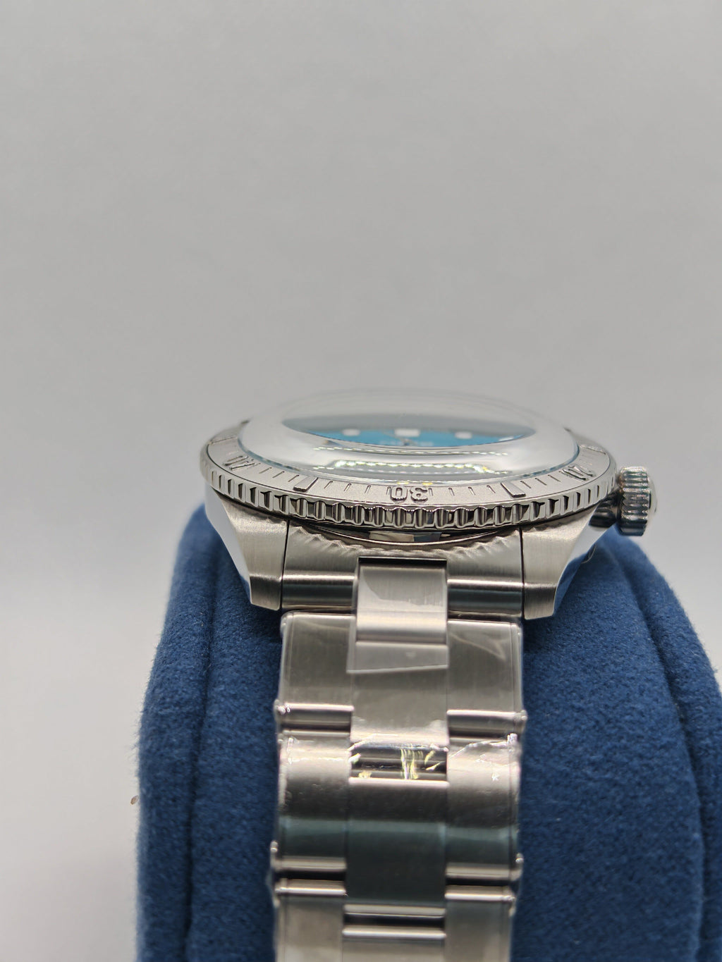 Cassa in acciaio con fondello marcato, bracciale su supporto blu, quadrante non visibile