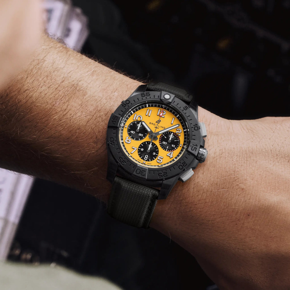 Orologio Breitling al polso, quadrante giallo con cronografi e cinturino nero a trama